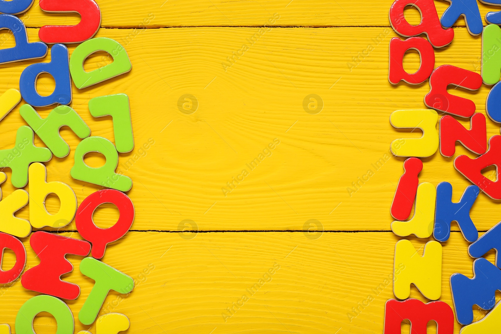 Photo of Learning alphabet. Magnetic letters on yellow wooden background, flat lay. Space for text