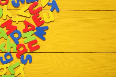 Learning alphabet. Magnetic letters on yellow wooden background, flat lay. Space for text