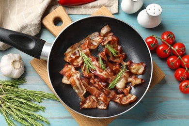 Delicious bacon slices in frying pan and products on light blue wooden table, flat lay