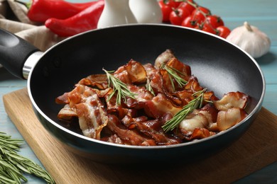 Delicious bacon slices in frying pan and products on light blue wooden table, closeup