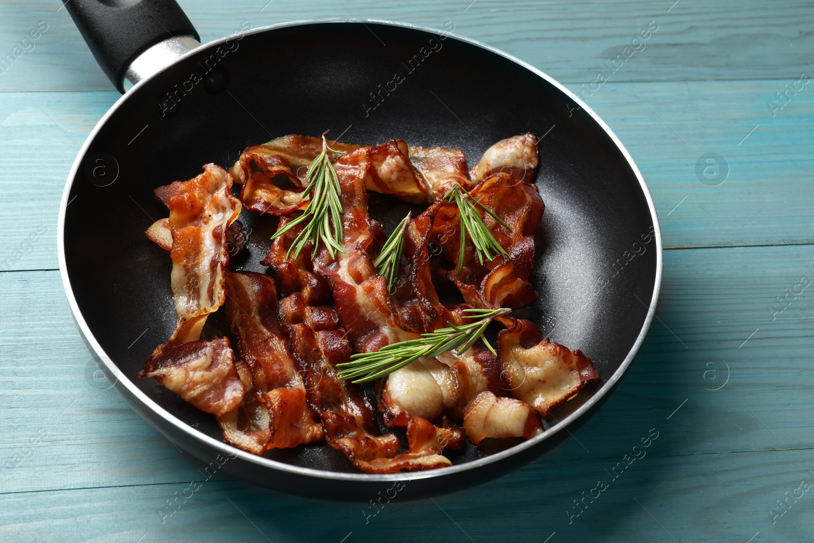 Photo of Delicious bacon slices in frying pan and rosemary on light blue wooden table