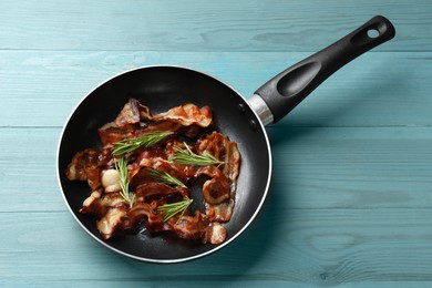 Photo of Delicious bacon slices in frying pan and rosemary on light blue wooden table, top view