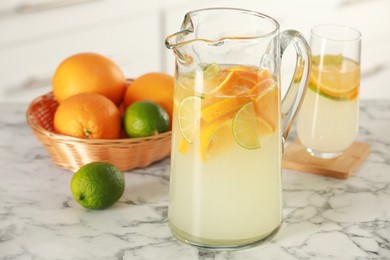 Photo of Refreshing lemonade with orange and lime in jug on white marble table