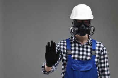 Photo of Worker in gas mask and helmet showing stop gesture on grey background. Space for text