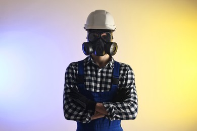 Photo of Worker in gas mask and helmet with crossed arms on color background