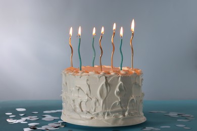 Tasty Birthday cake with burning candles and confetti on light blue table against gray background