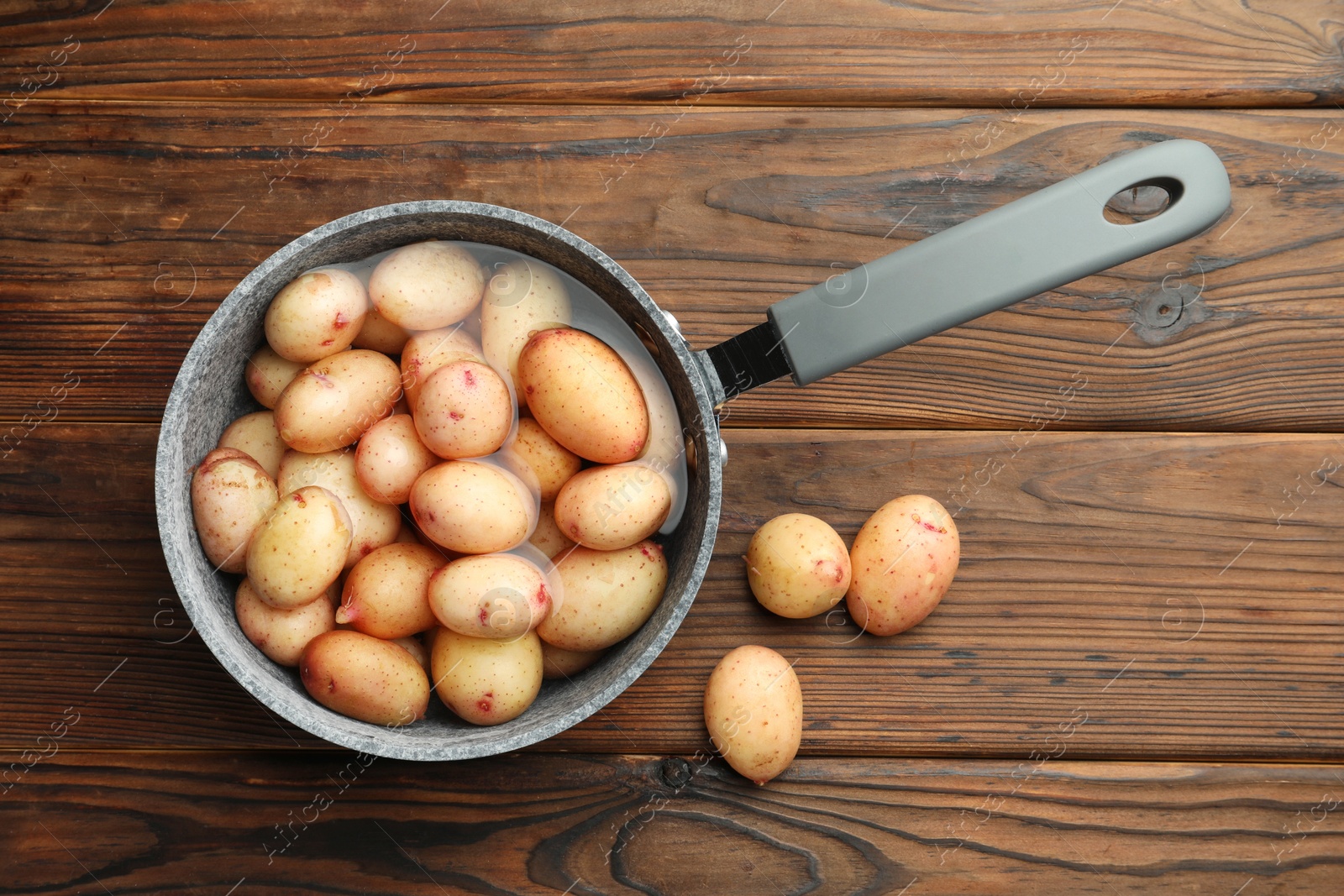 Photo of Raw potatoes in saucepan with water on wooden table, top view