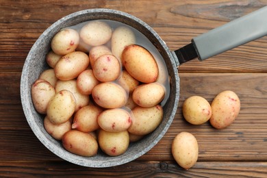 Raw potatoes in saucepan with water on wooden table, top view