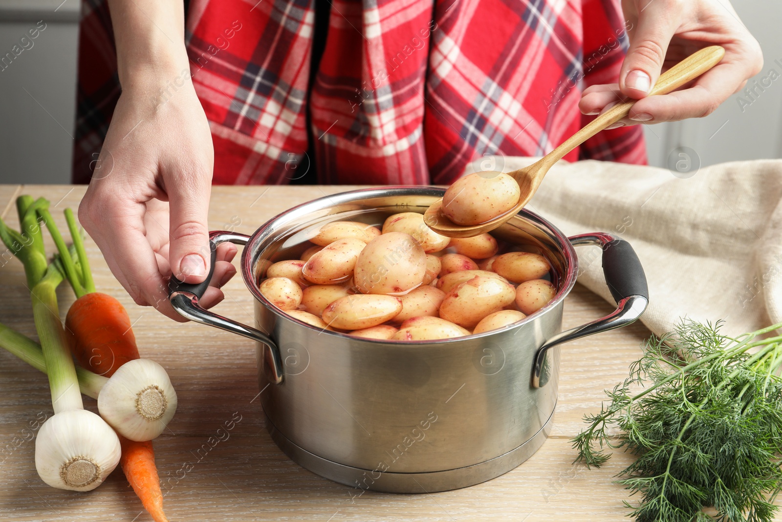 Photo of Woman taking raw potato from pot with water at table, closeup