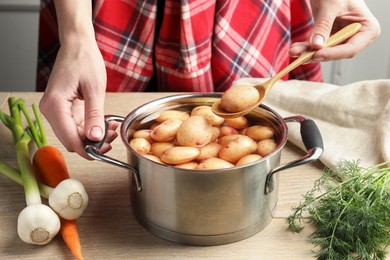 Woman taking raw potato from pot with water at table, closeup