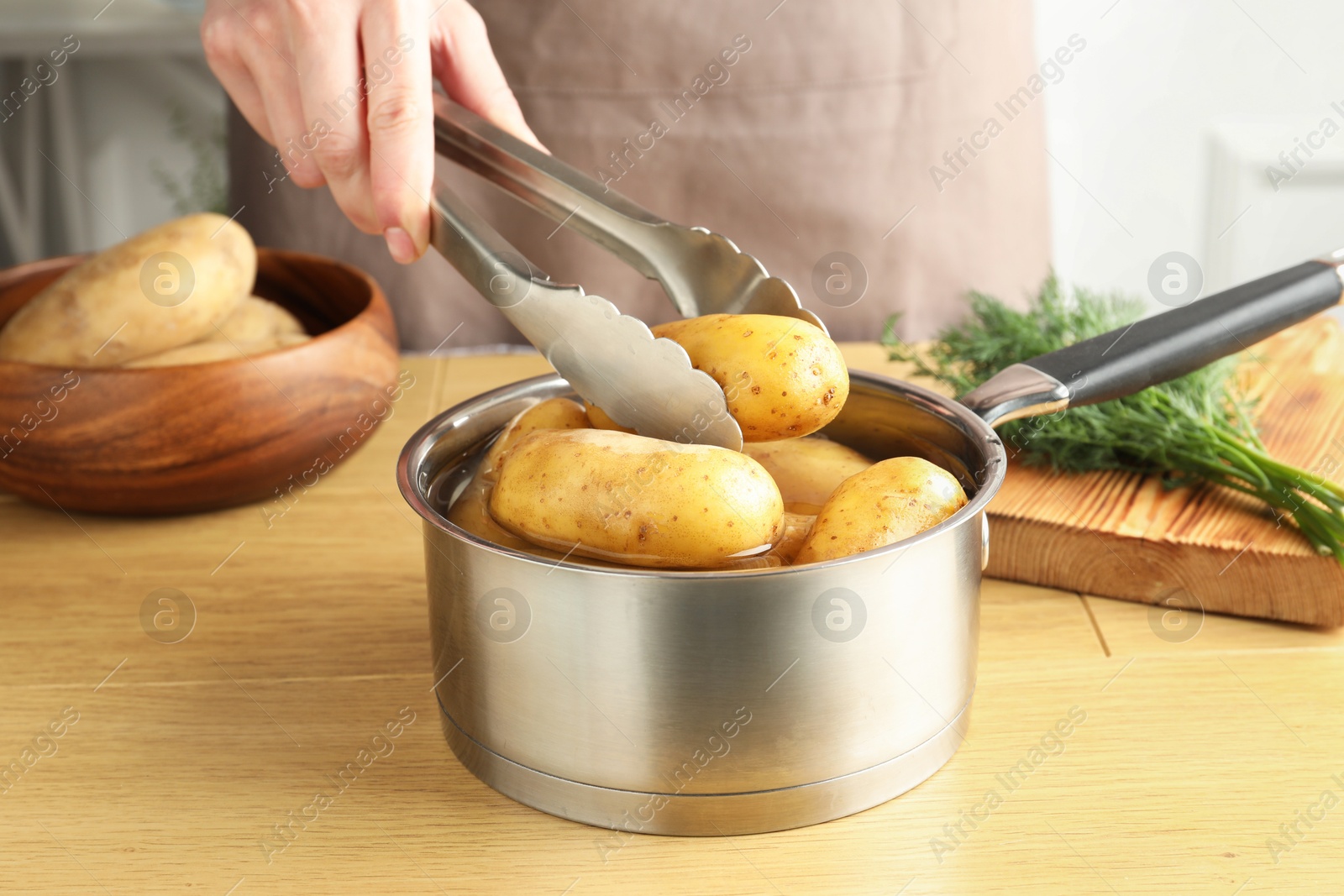 Photo of Woman putting raw potato into saucepan at wooden table, closeup