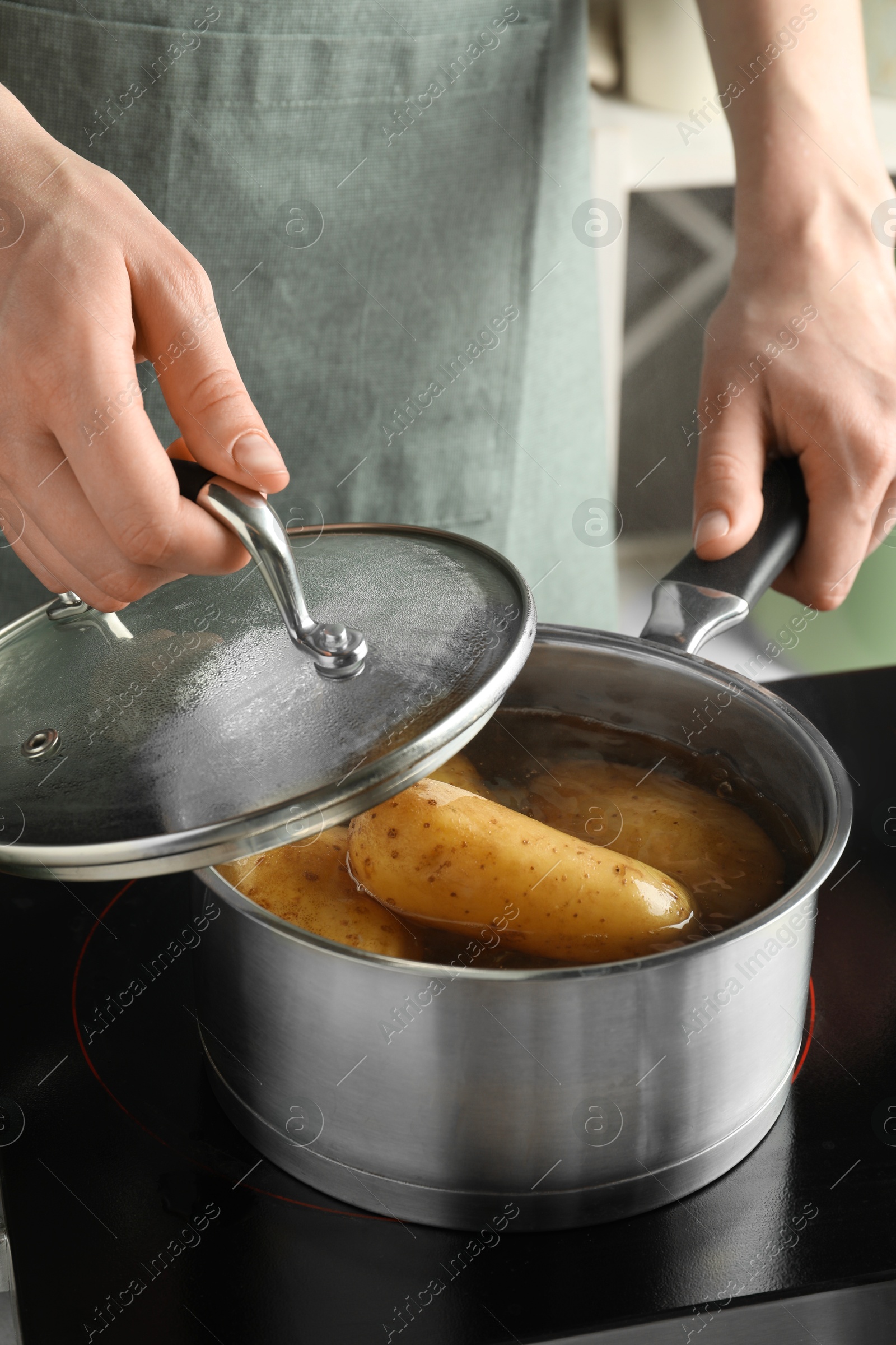 Photo of Woman boiling potatoes in saucepan on stove, closeup