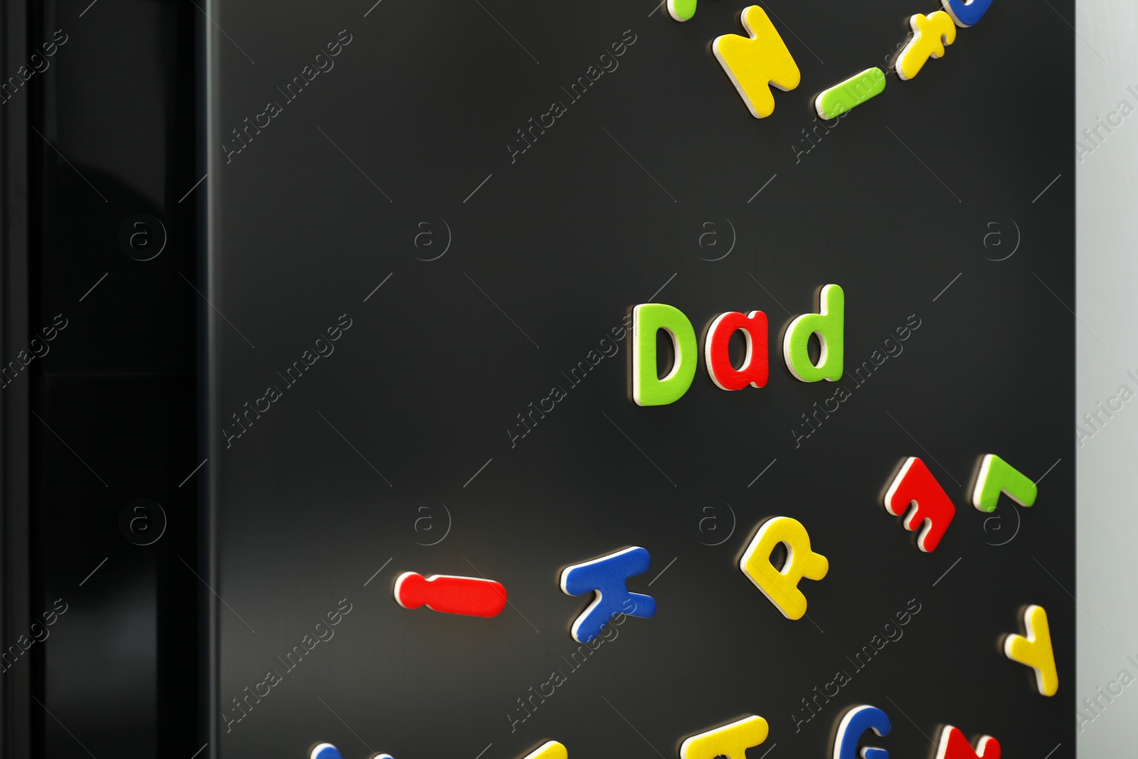 Photo of Word Dad made of many bright magnetic letters on fridge indoors. Learning alphabet