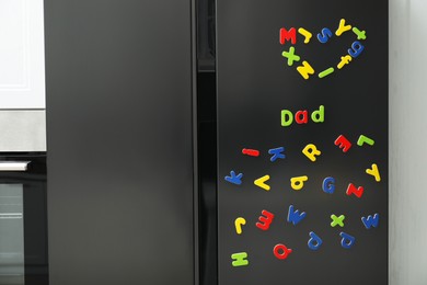 Photo of Word Dad and heart made of many bright magnetic letters on fridge indoors. Learning alphabet