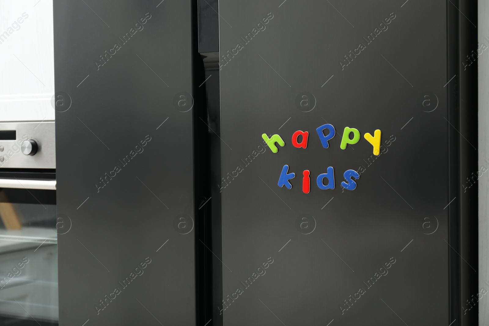 Photo of Words Happy Kids made of bright magnetic letters on fridge indoors. Learning alphabet