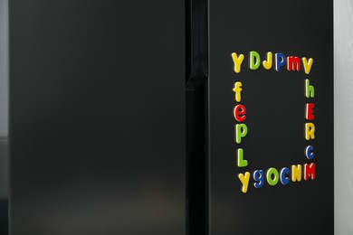 Photo of Frame made of many bright magnetic letters on fridge indoors. Learning alphabet