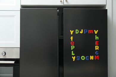 Frame made of many bright magnetic letters on fridge indoors. Learning alphabet