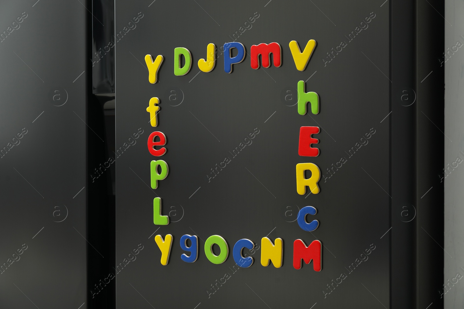 Photo of Frame made of many bright magnetic letters on fridge indoors. Learning alphabet