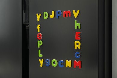 Frame made of many bright magnetic letters on fridge indoors. Learning alphabet