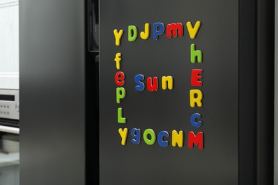 Photo of Word Sun and frame made of many bright magnetic letters on fridge indoors. Learning alphabet