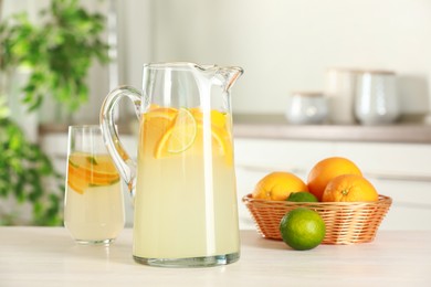 Refreshing lemonade with orange and lime in jug on white wooden table