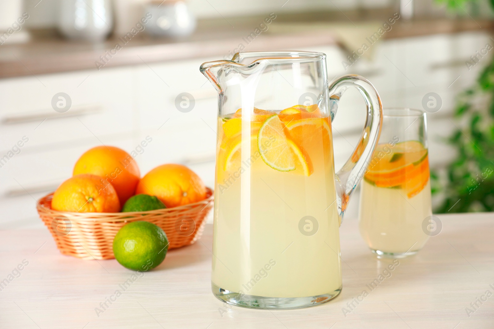 Photo of Refreshing lemonade with orange and lime in jug on white wooden table