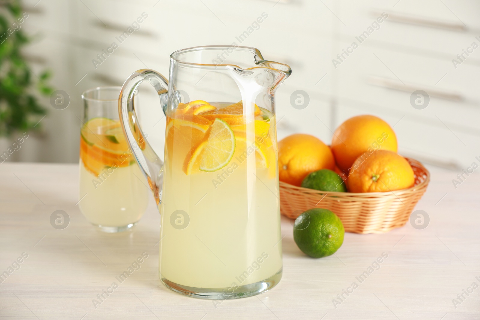 Photo of Refreshing lemonade with orange and lime in jug on white wooden table