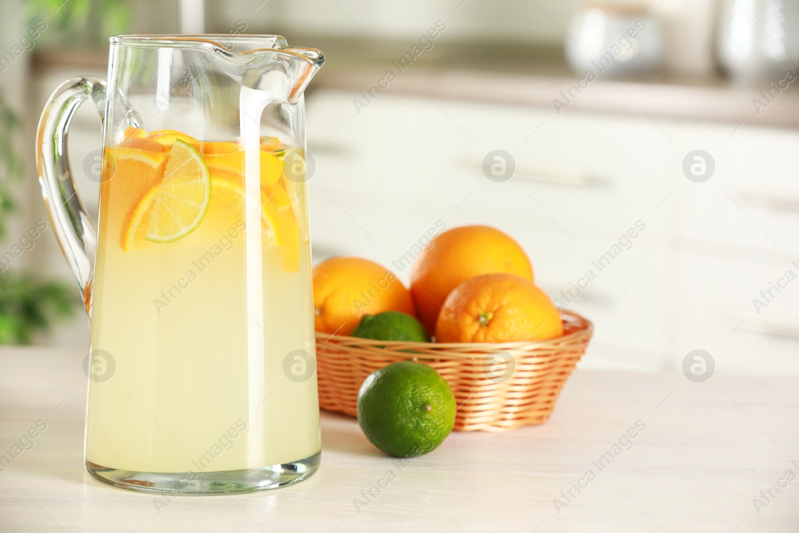 Photo of Refreshing lemonade with orange and lime in jug on white wooden table. Space for text