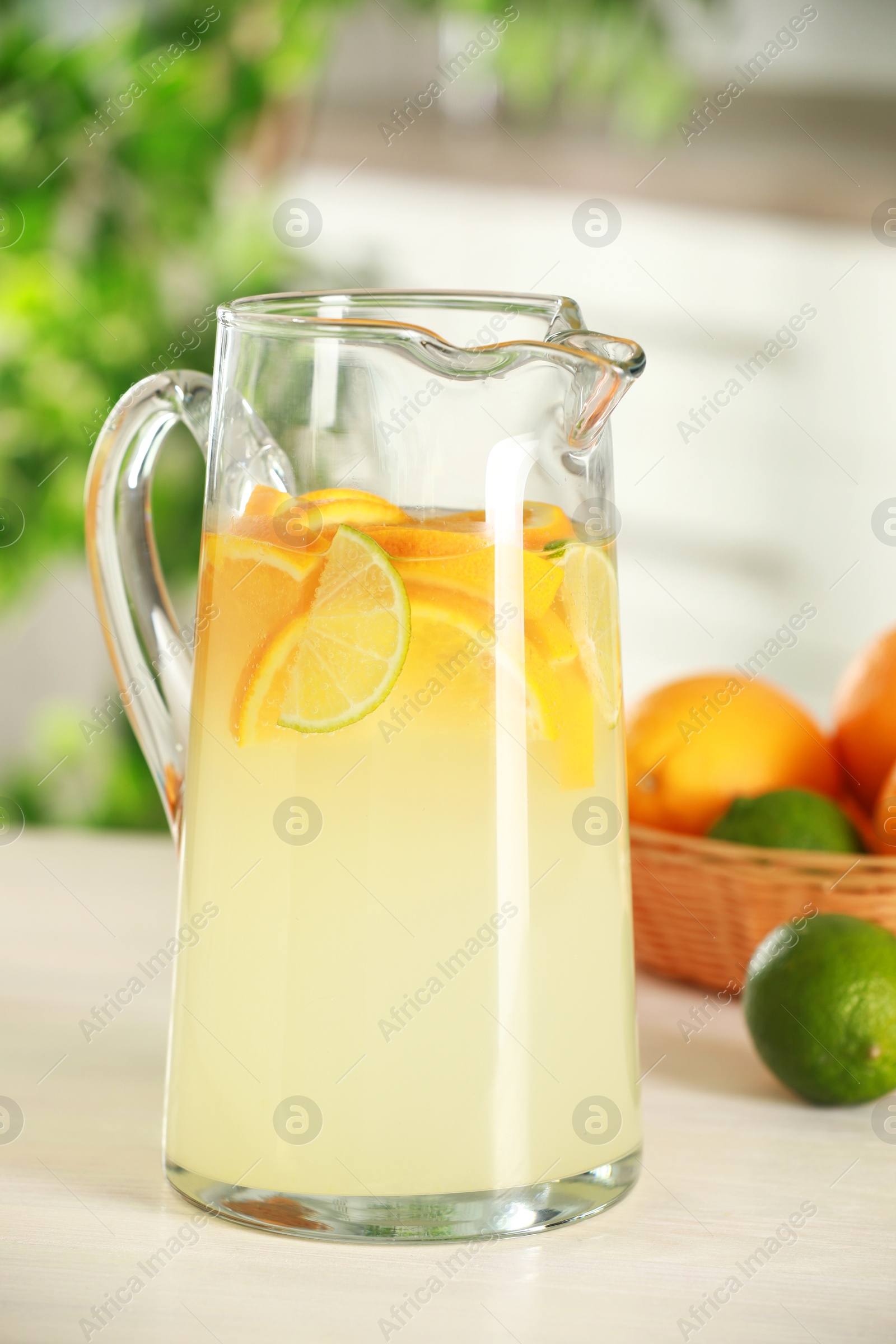 Photo of Refreshing lemonade with orange and lime in jug on white wooden table, closeup