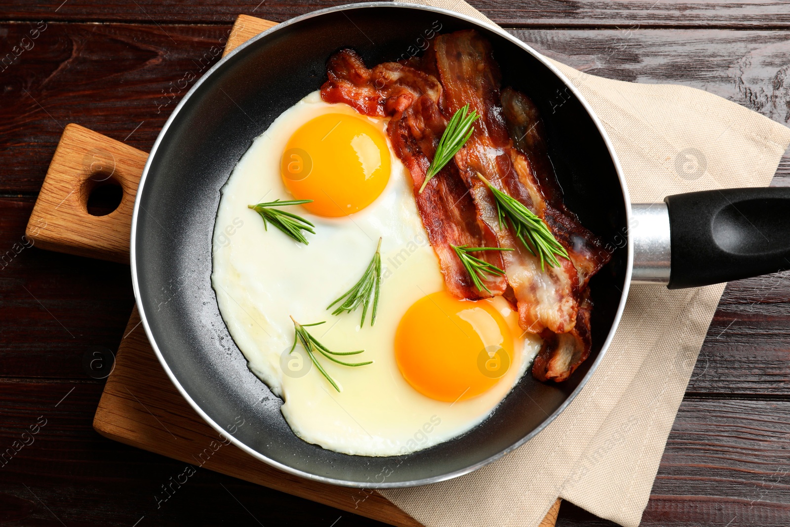 Photo of Tasty bacon, eggs and rosemary in frying pan on wooden table, top view