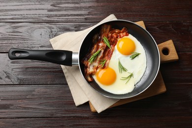 Photo of Tasty bacon, eggs and rosemary in frying pan on wooden table, top view