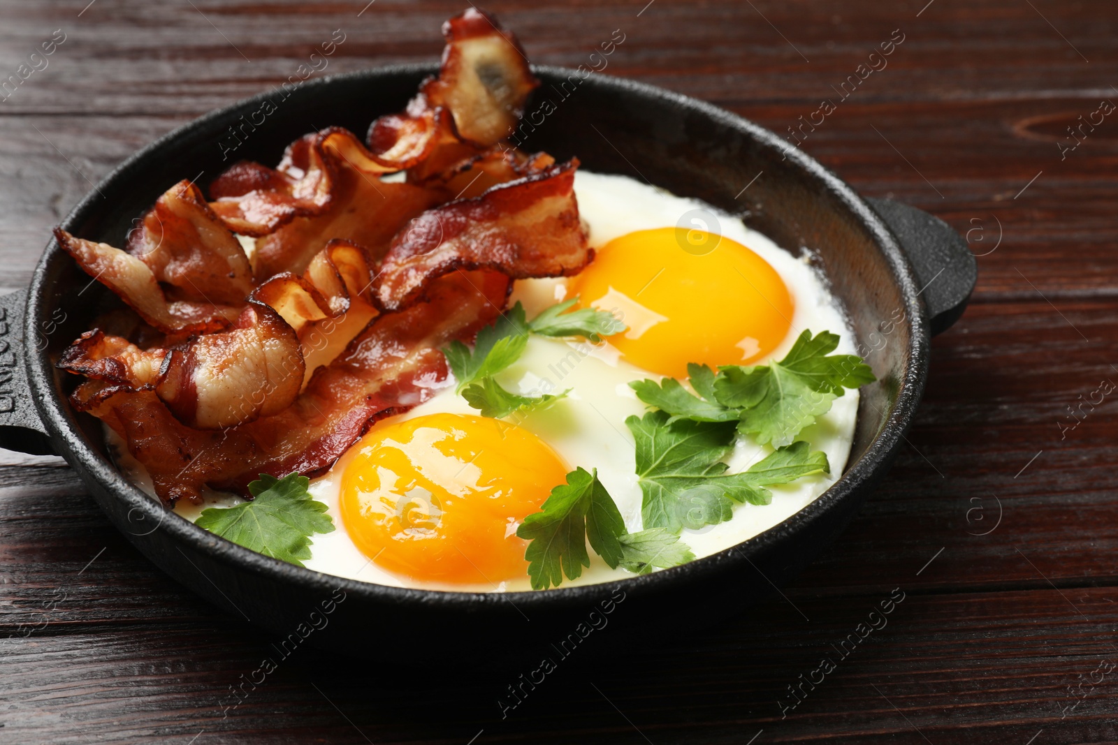 Photo of Tasty bacon, eggs and parsley in frying pan on wooden table, closeup