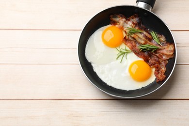 Tasty bacon, eggs and rosemary in frying pan on light wooden table, top view. Space for text