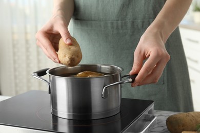 Photo of Woman putting potato into metal pot on stove, closeup