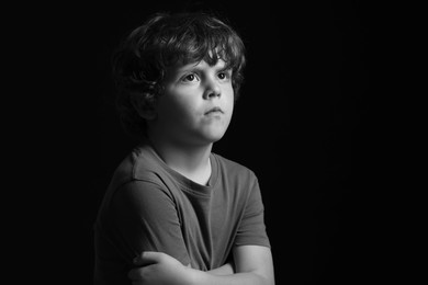 Portrait of sad little boy on dark background, space for text. Black and white effect