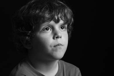 Portrait of sad little boy on dark background. Black and white effect