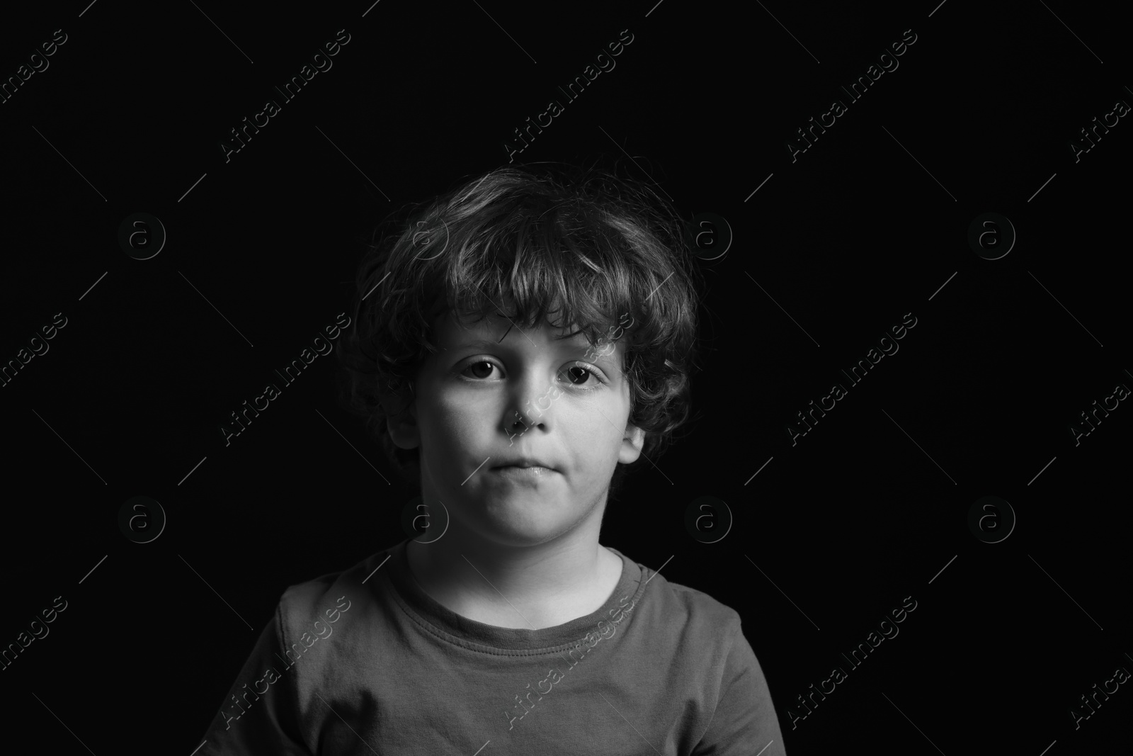 Photo of Portrait of sad little boy on dark background. Black and white effect