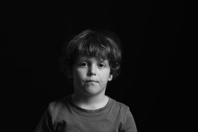 Photo of Portrait of sad little boy on dark background. Black and white effect