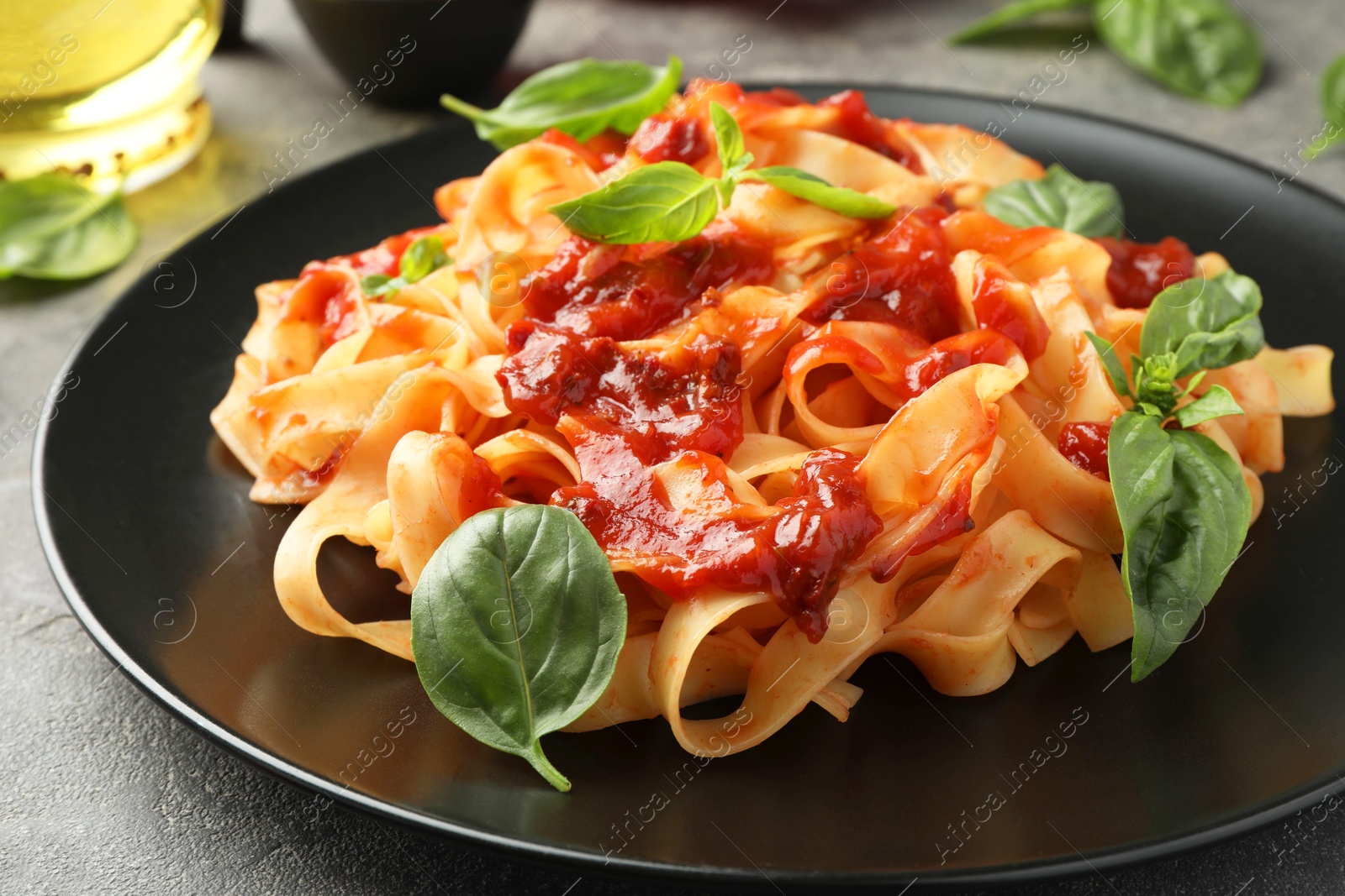 Photo of Delicious pasta with tomato sauce and basil on grey table, closeup