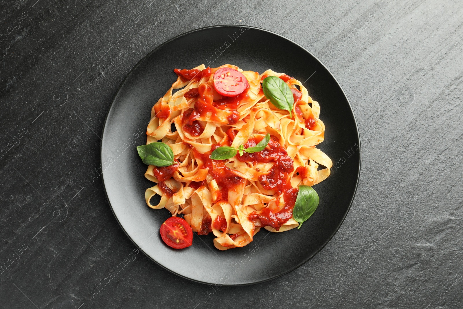 Photo of Delicious pasta with tomato sauce, vegetable and basil on dark textured table, top view