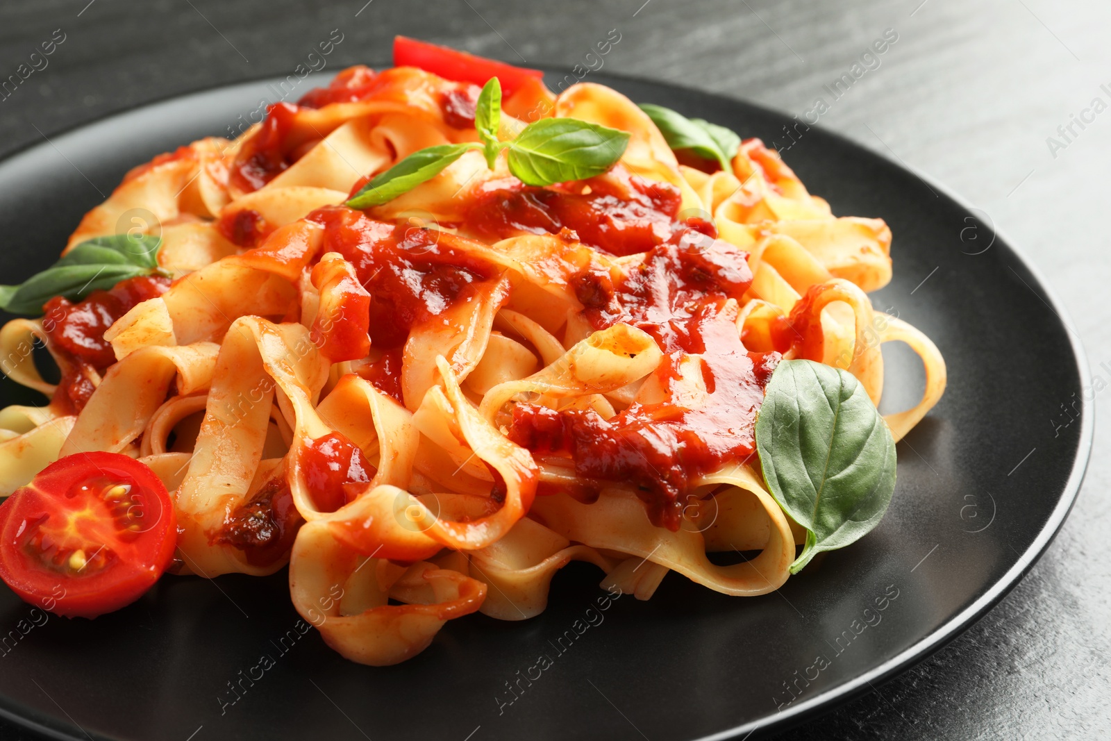 Photo of Delicious pasta with tomato sauce, vegetable and basil on dark textured table, closeup