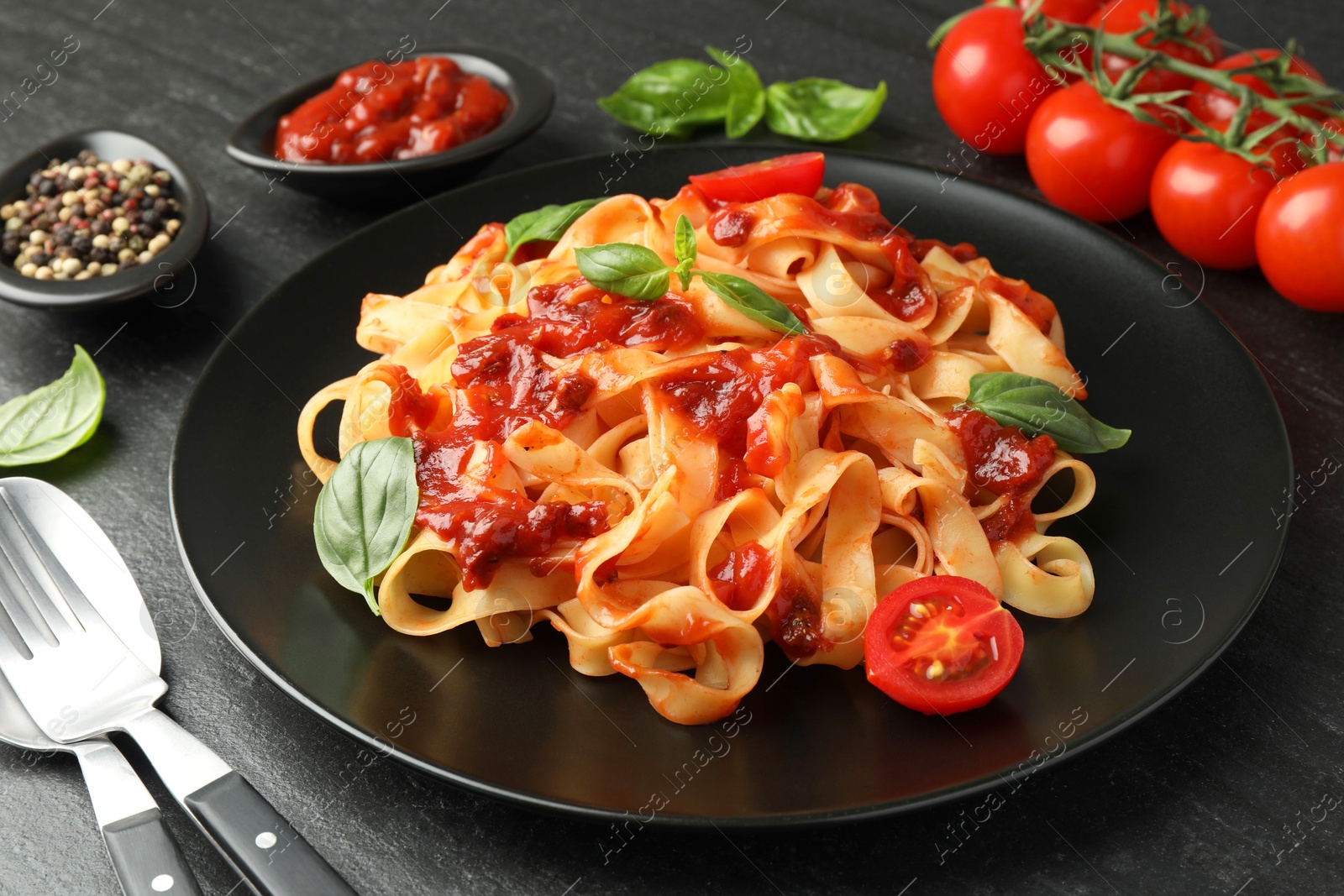 Photo of Delicious pasta with tomato sauce, vegetable, basil and spices served on dark textured table, closeup