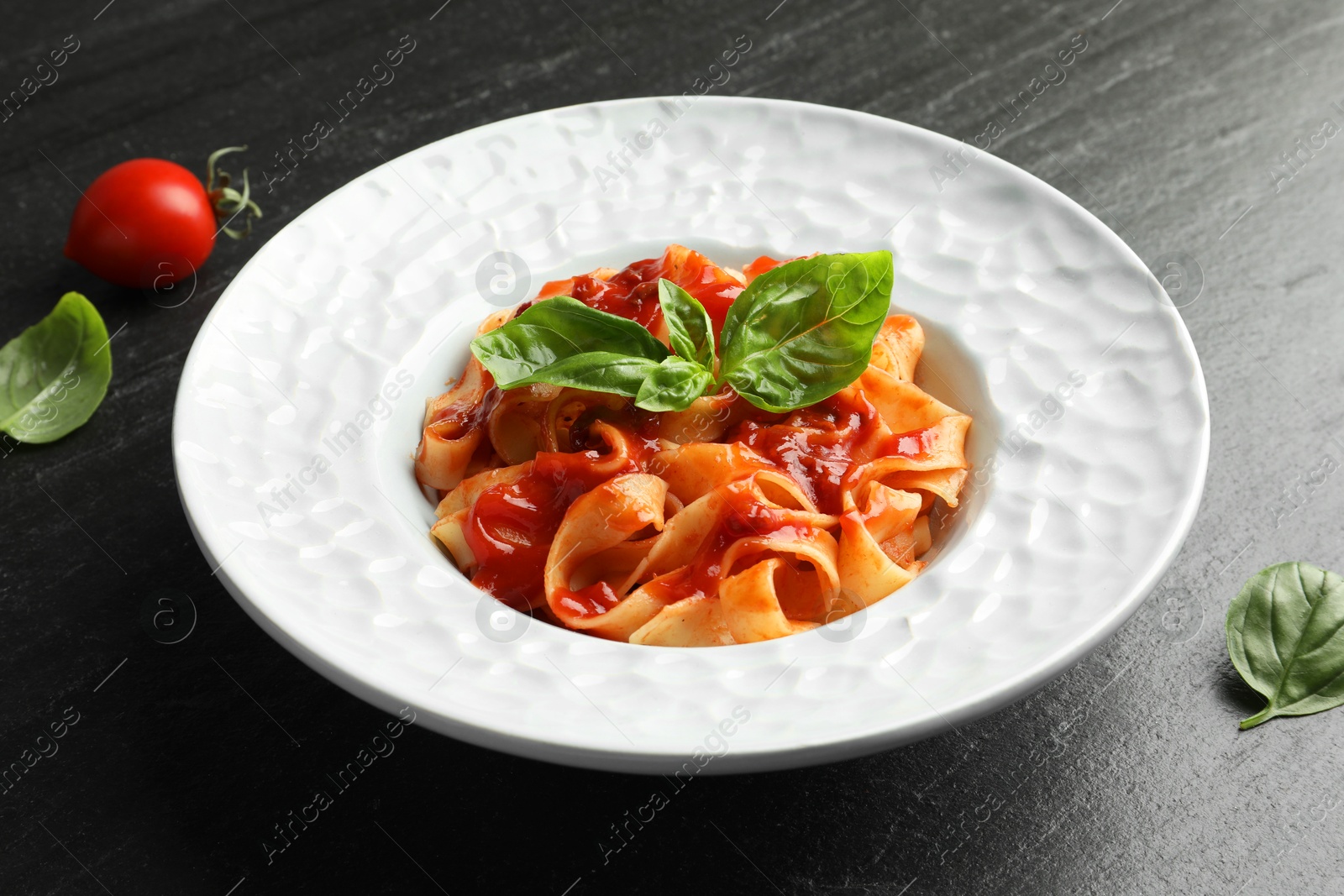 Photo of Delicious pasta with tomato sauce and basil on dark textured table, closeup