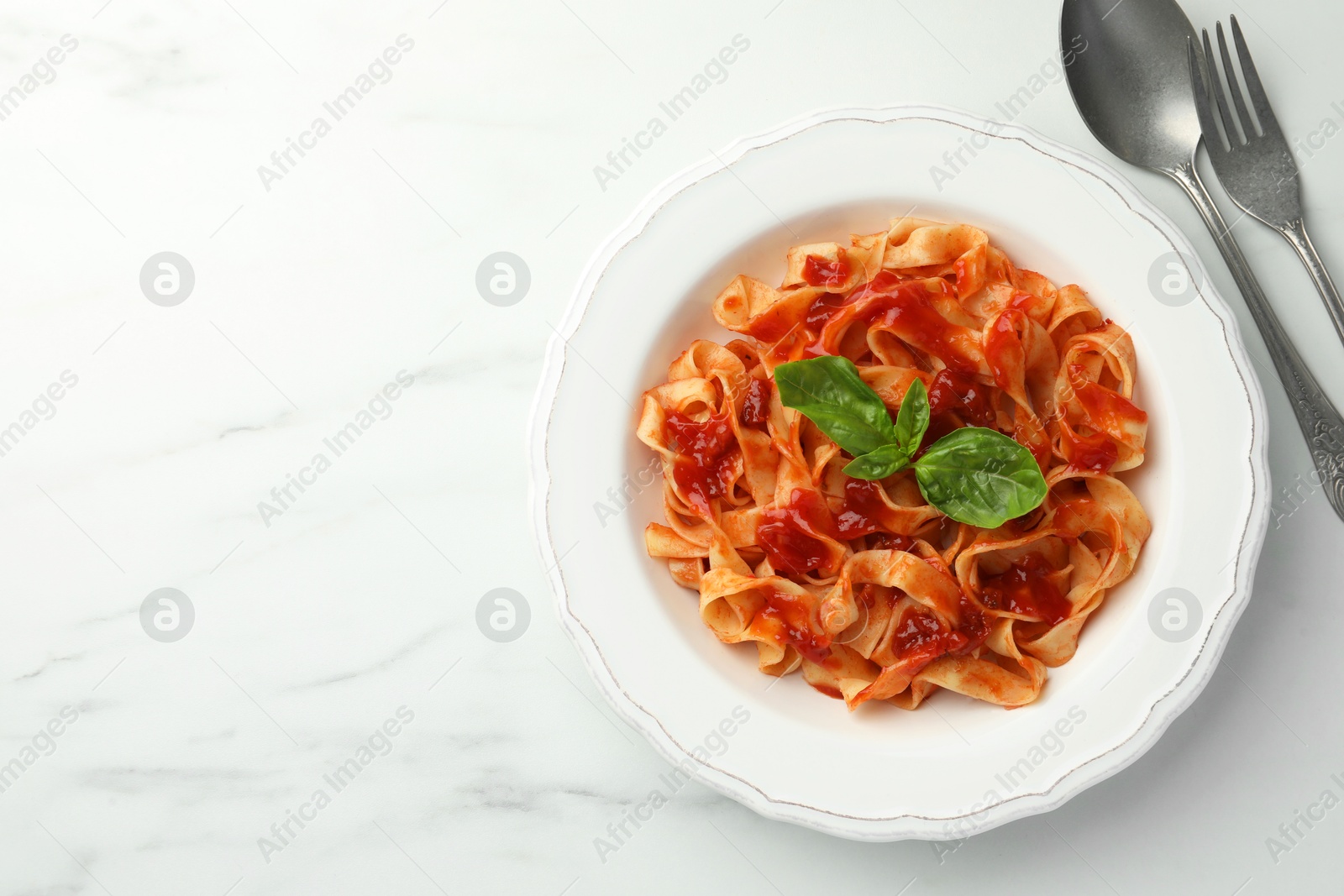 Photo of Delicious pasta with tomato sauce and basil served on white marble table, flat lay. Space for text