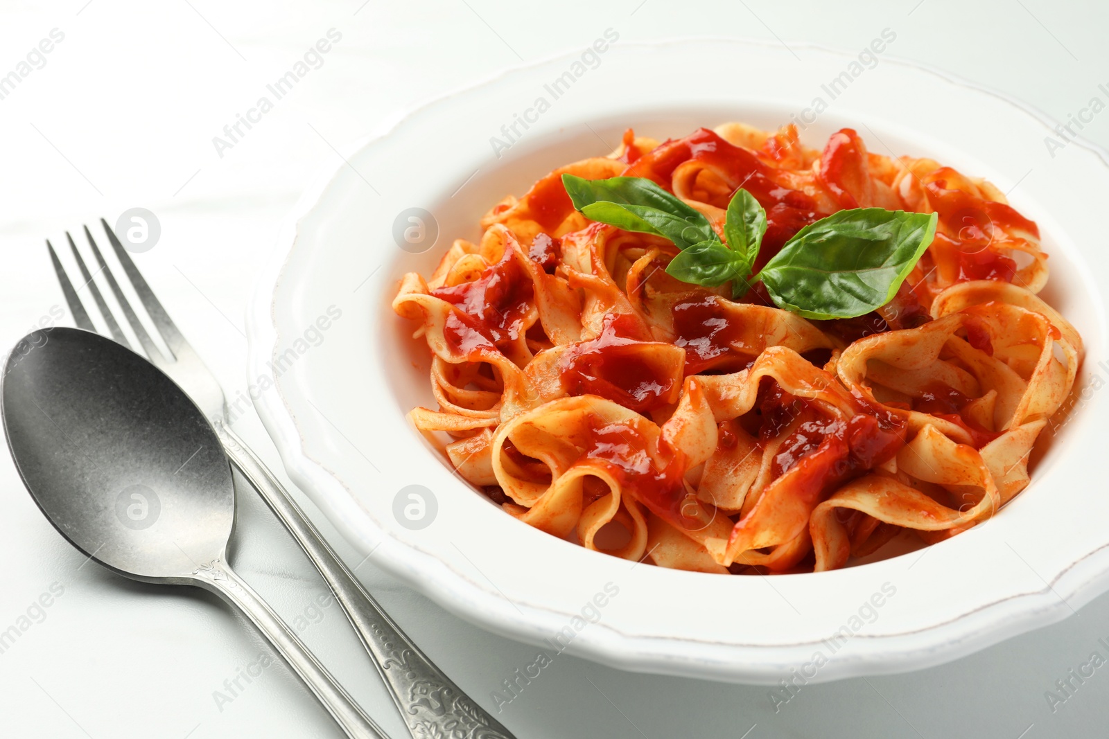 Photo of Delicious pasta with tomato sauce and basil served on white marble table, closeup