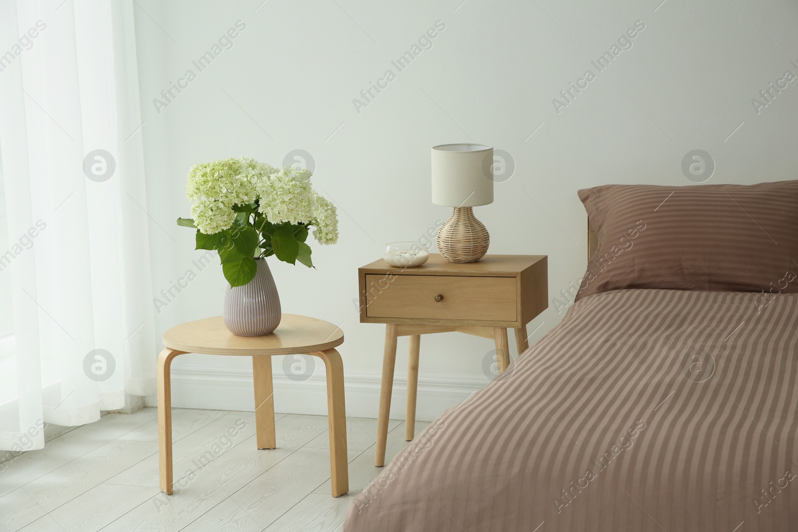 Photo of Stylish bedroom interior with comfortable bed, bouquet of flowers and bedside table