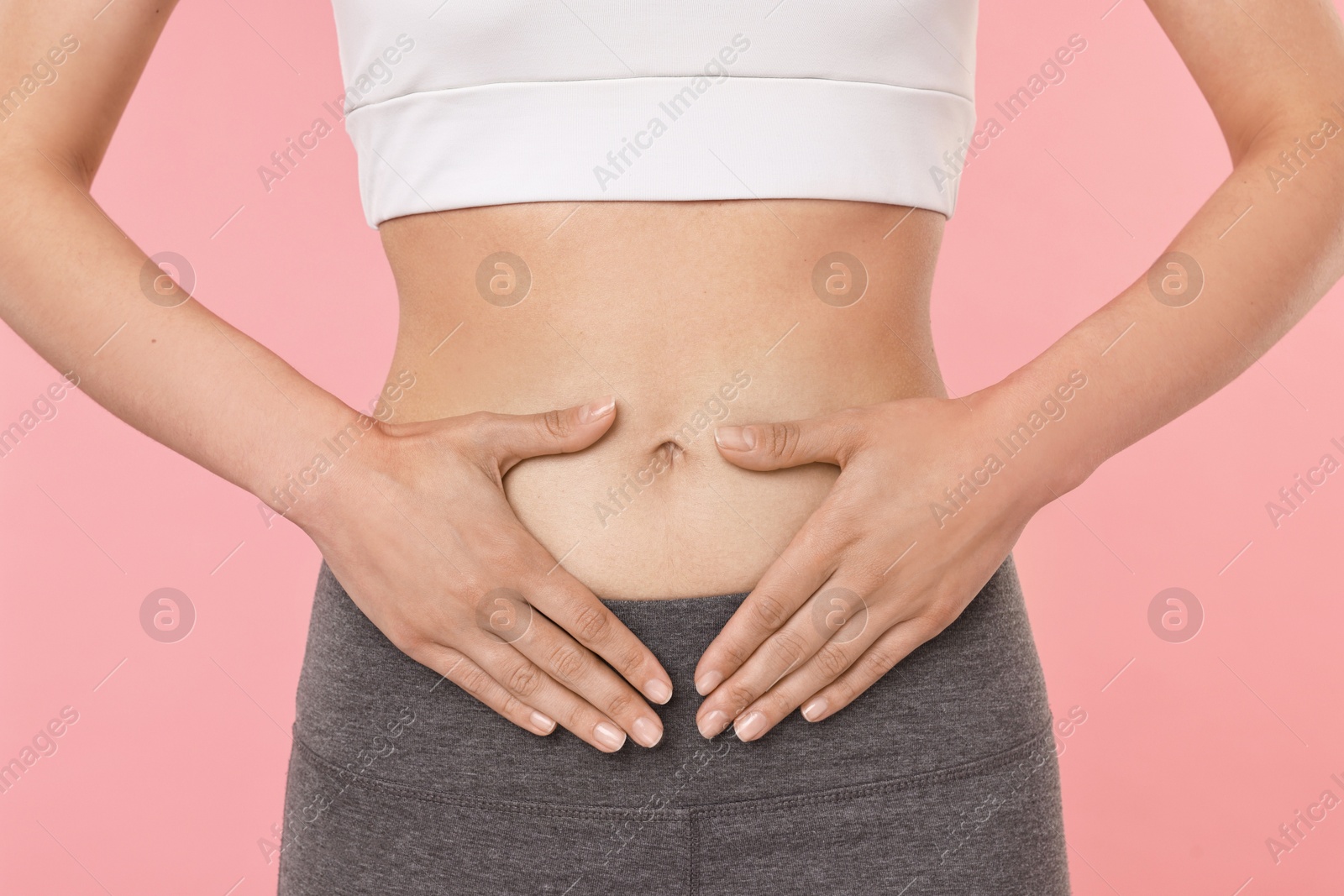 Photo of Healthy digestion. Woman making heart shape with hands near her belly on pink background, closeup