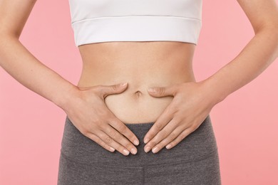 Photo of Healthy digestion. Woman making heart shape with hands near her belly on pink background, closeup