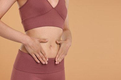 Photo of Healthy digestion. Woman touching her belly on beige background, closeup. Space for text