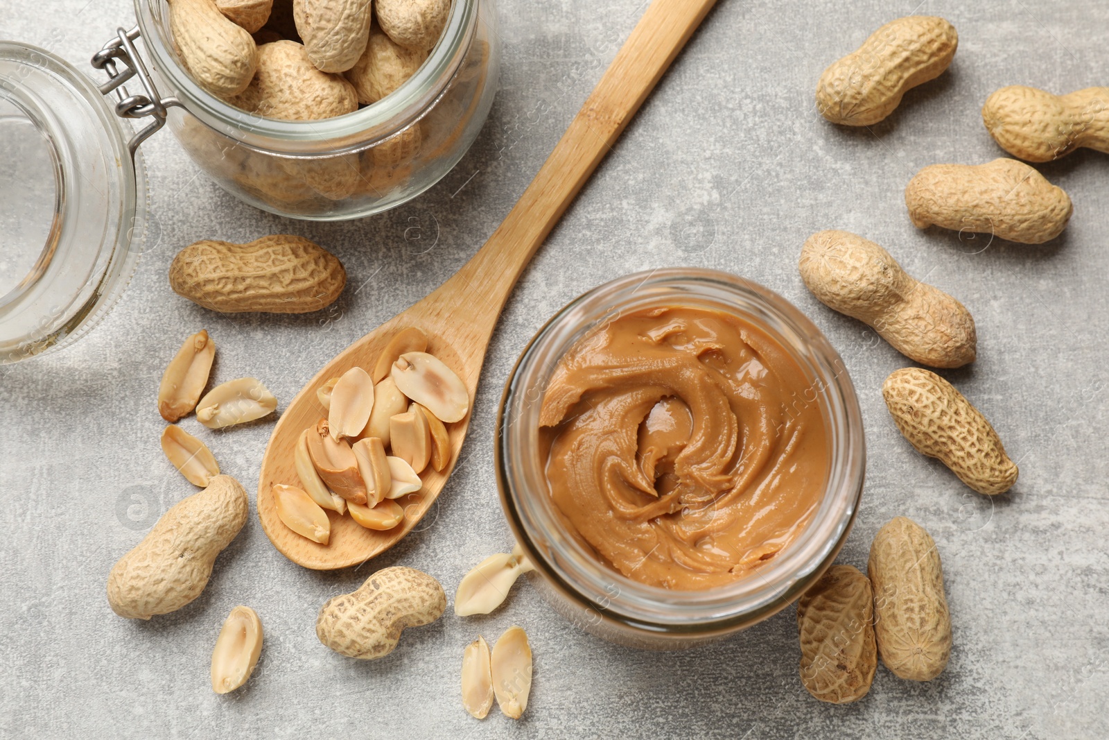 Photo of Tasty peanut butter in jar and groundnuts on grey textured table, flat lay